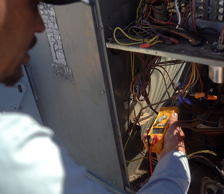 A person uses a digital multimeter to test electrical wires inside an open control panel, inspecting or repairing the system for Viking HVAC, a top-rated Phoenix HVAC contractor. The scene appears to be outdoors in daylight.